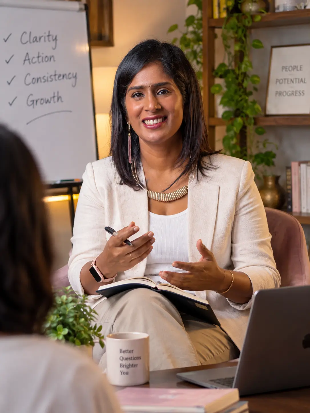 Dr. Indhu Nagaiah in a cream blazer, smiling and gesturing warmly during a coaching conversation