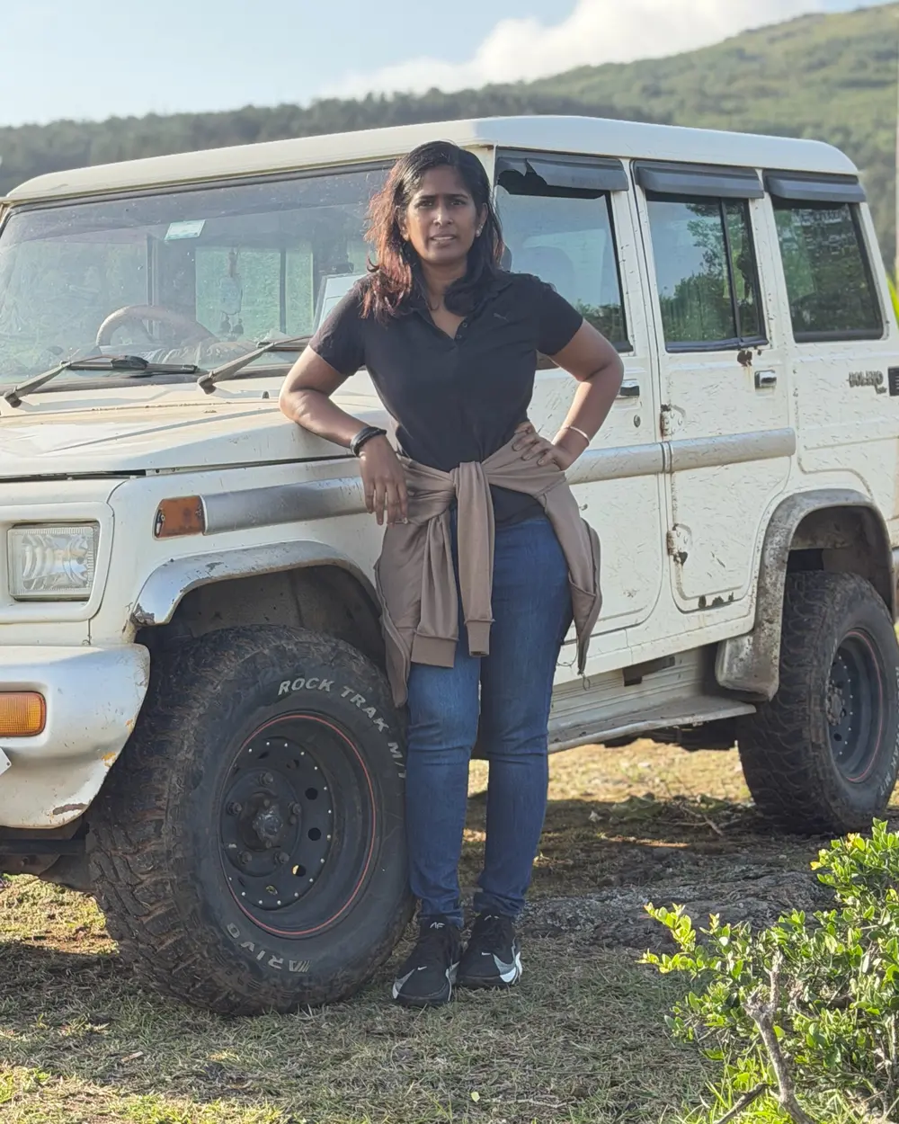 Dr. Indhu Nagaiah leaning against a white four-wheel drive in the green hills of the Nilgiris