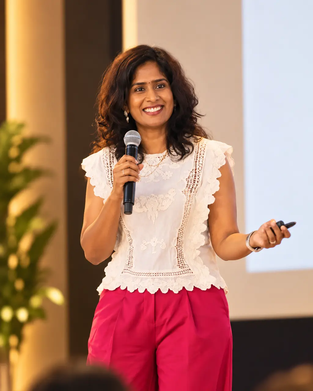 Dr. Indhu Nagaiah speaking on stage with a microphone, smiling at the audience
